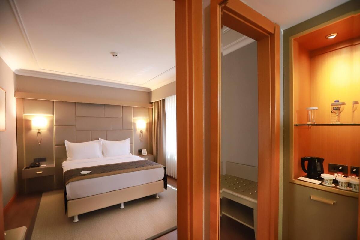 Ein Hotelzimmer mit Bett, Nachttischen, Schreibtisch, Stuhl, Ablagefläche für Kosmetika und Spiegel.