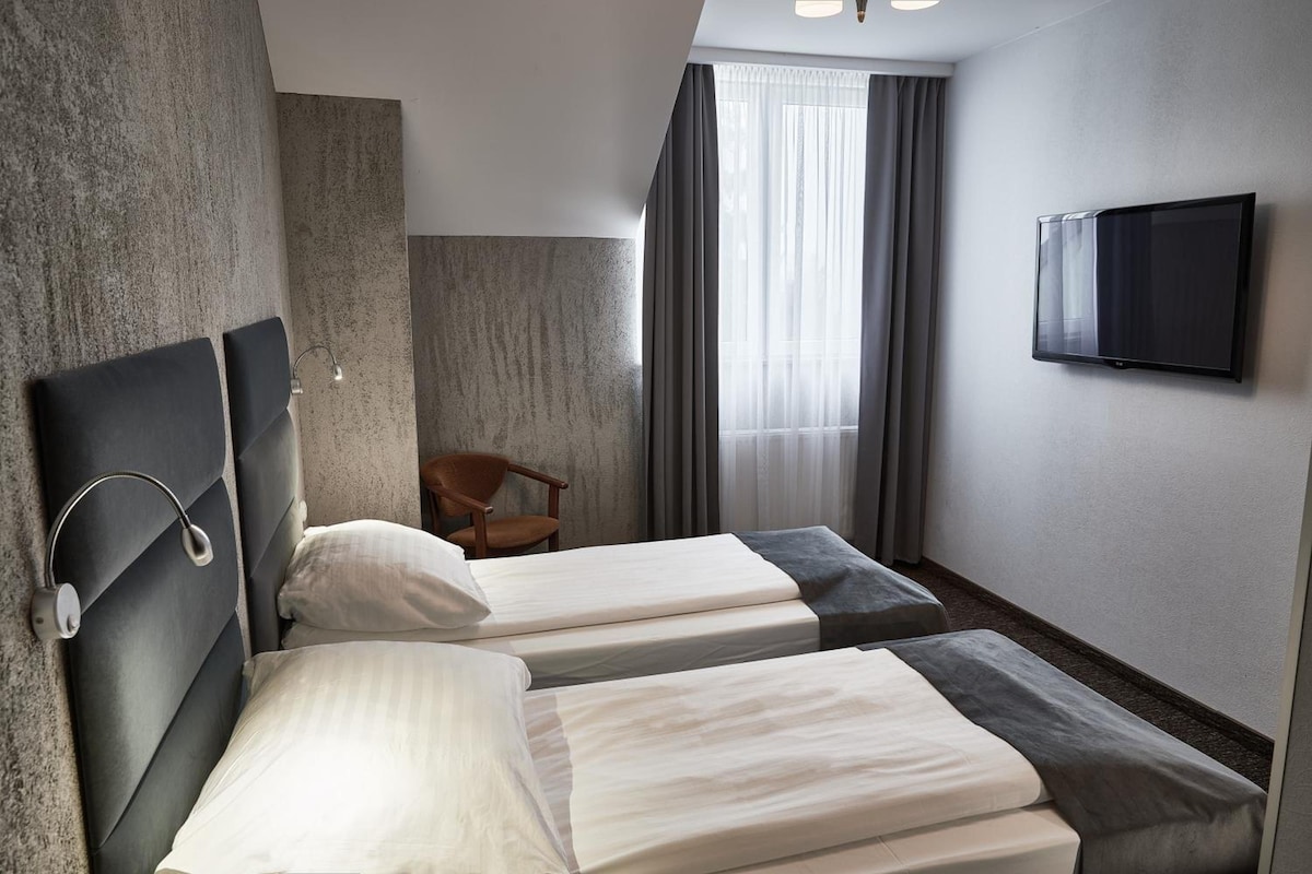 A hotel room with two beds, a television, a chair, and a window with curtains.