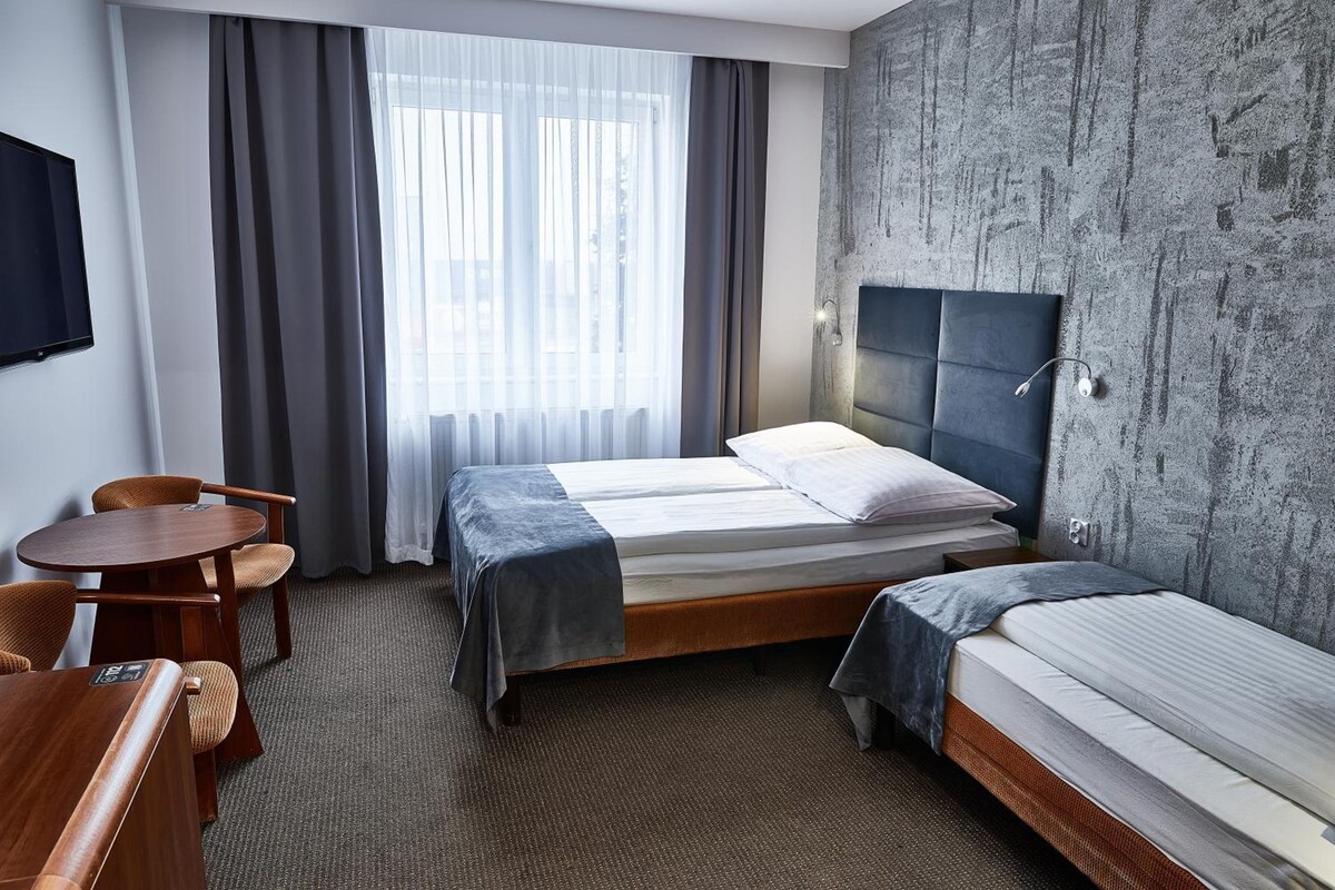 A hotel room with a bed, a desk, a chair, and a large window with curtains.