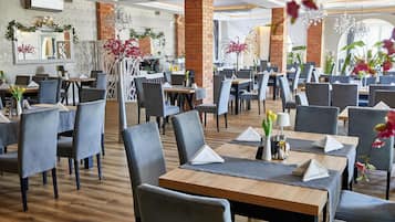 A restaurant with multiple tables and chairs, brick walls, and decorative plants.