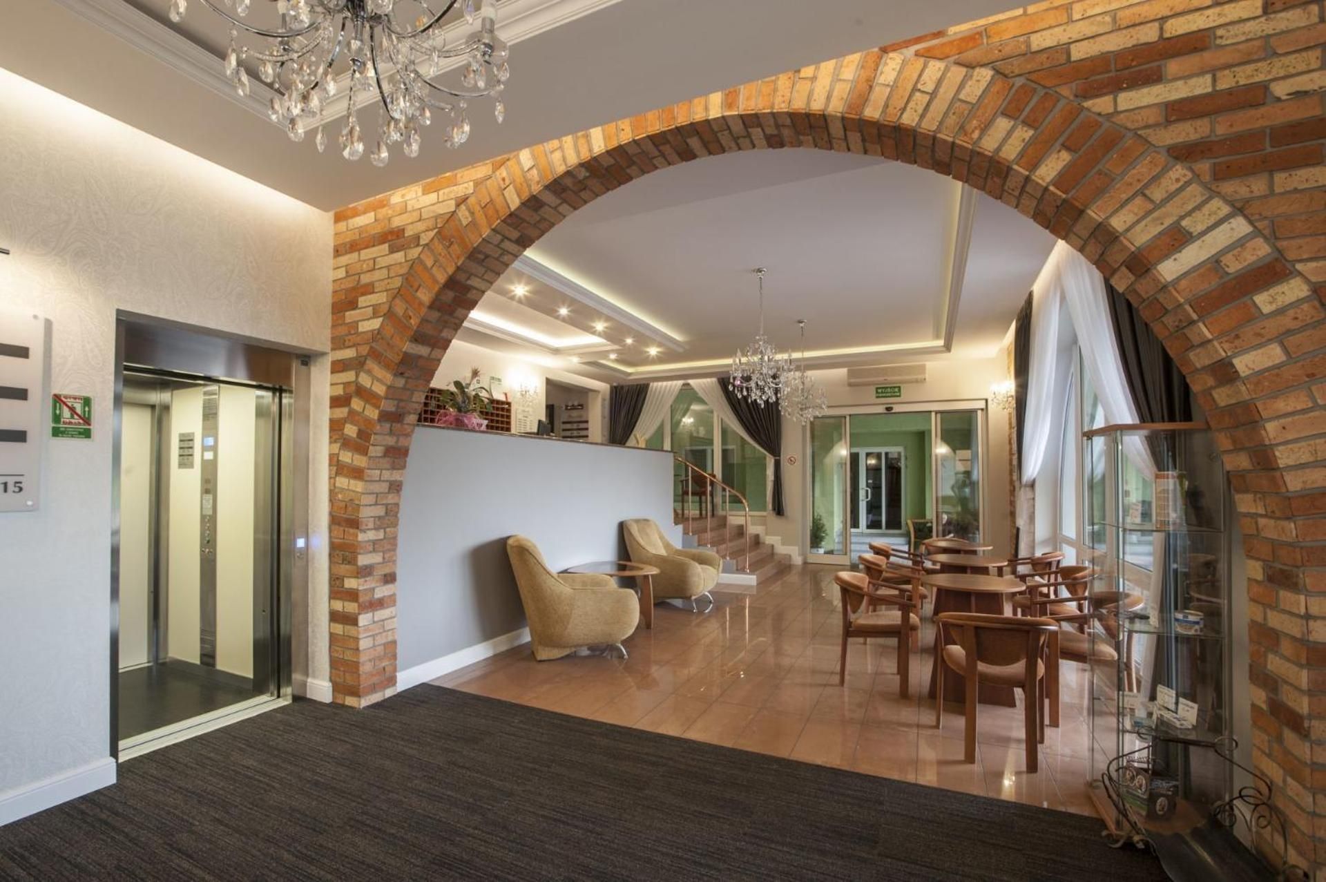 A hotel lobby with a brick archway, a reception desk, a chandelier, and a seating area with tables and chairs.