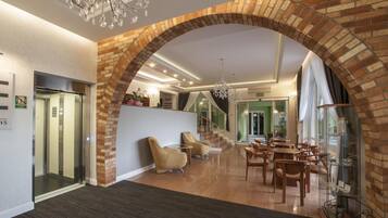 A hotel lobby with a brick archway, a reception desk, a chandelier, and a seating area with tables and chairs.