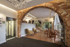 A hotel lobby with a brick archway, a reception desk, a chandelier, and a seating area with tables and chairs.