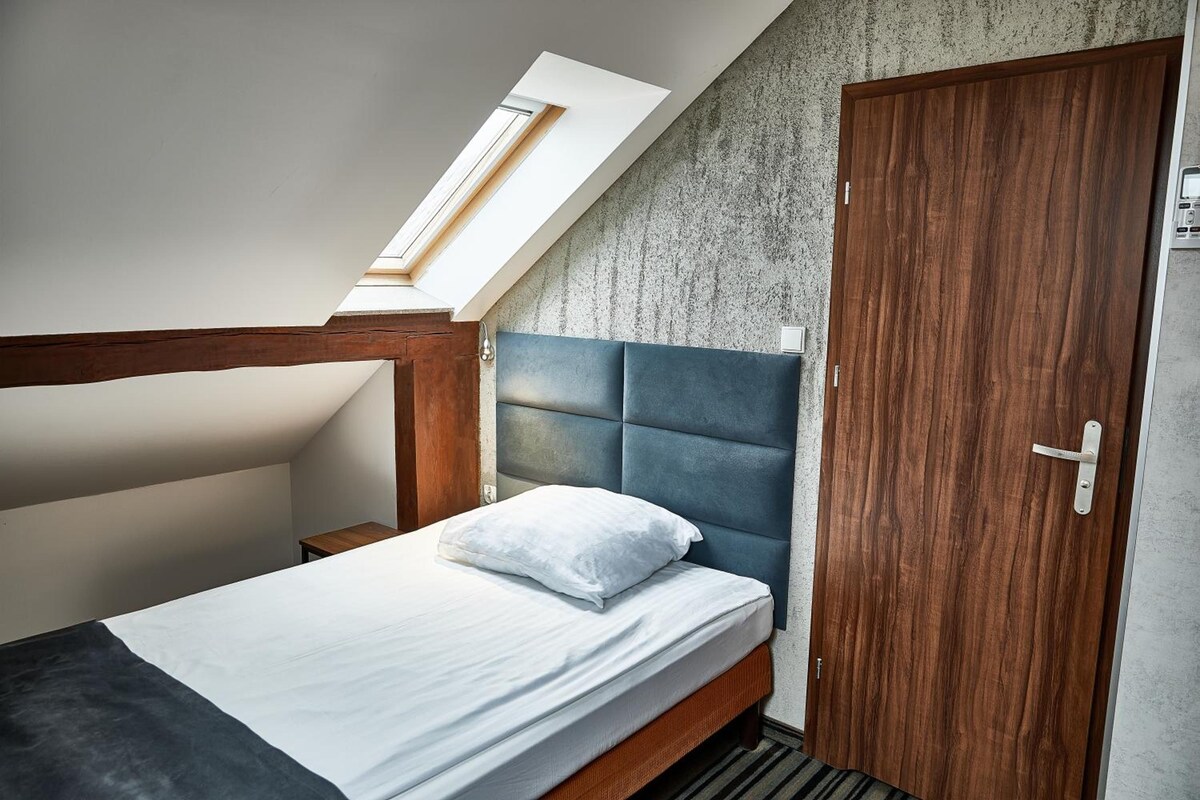 A bedroom with a sloped ceiling, a bed with a headboard, a wooden wardrobe, and a small table.