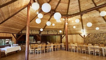 A rustic wooden hall with a high ceiling, multiple tables and chairs, and hanging spherical light fixtures.