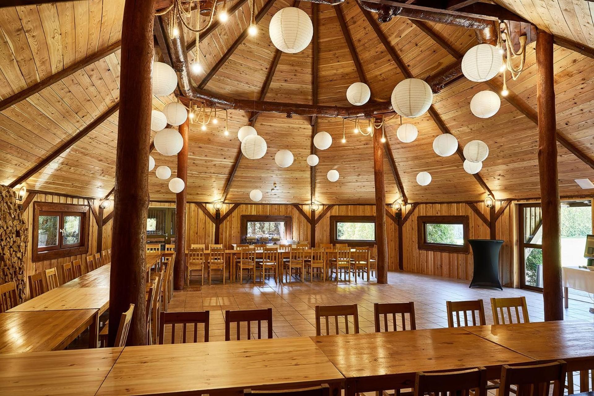 A spacious wooden dining area with multiple tables and chairs, large windows, and hanging paper lanterns.