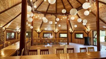 A spacious wooden dining area with multiple tables and chairs, large windows, and hanging paper lanterns.