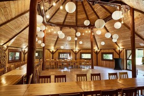 A spacious wooden dining area with multiple tables and chairs, large windows, and hanging paper lanterns.