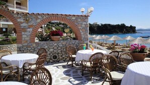 Un espace extérieur aménagé avec des arches en pierre, des chaises et des tables en osier, offrant une vue sur une plage et la mer.