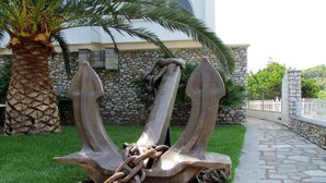 Une sculpture représentant trois ancres reliées par des chaînes, située dans un espace aménagé avec un palmier et un mur de pierres.