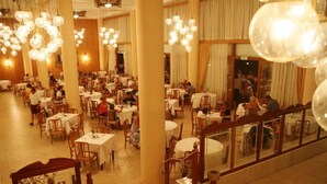 Un vaste espace dédié à la salle à manger, avec de nombreuses tables et chaises, de grandes colonnes et des luminaires suspendus.