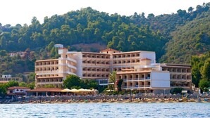 Un hôtel à plusieurs étages, une plage au premier plan et une colline en arrière-plan.