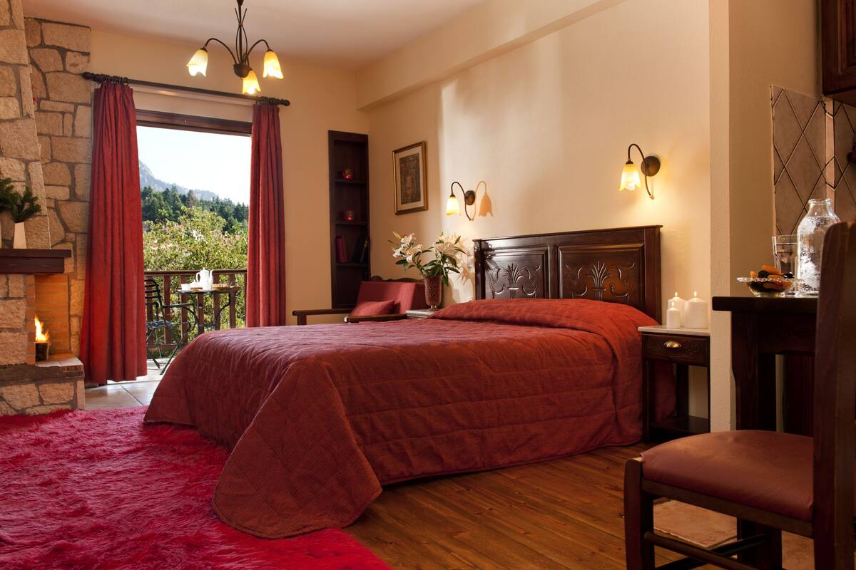 A bedroom with a large bed, a fireplace, a balcony with a view, and a nightstand with candles.