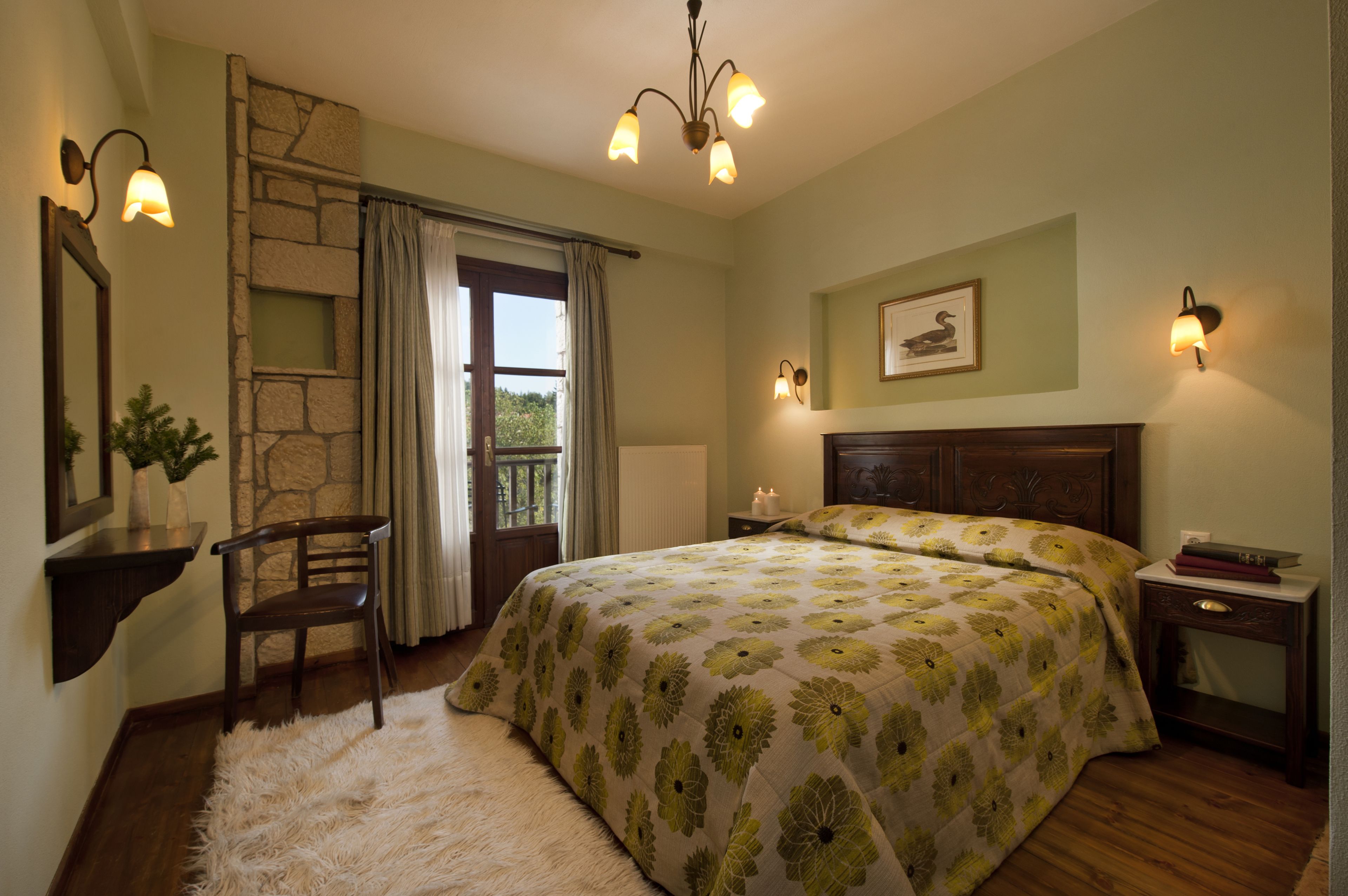 A bedroom with a large bed, a stone accent wall, a wooden nightstand, a chair, and a window with curtains.