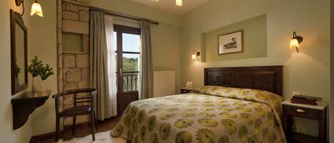 A bedroom with a large bed, a stone accent wall, a wooden nightstand, a chair, and a window with curtains.