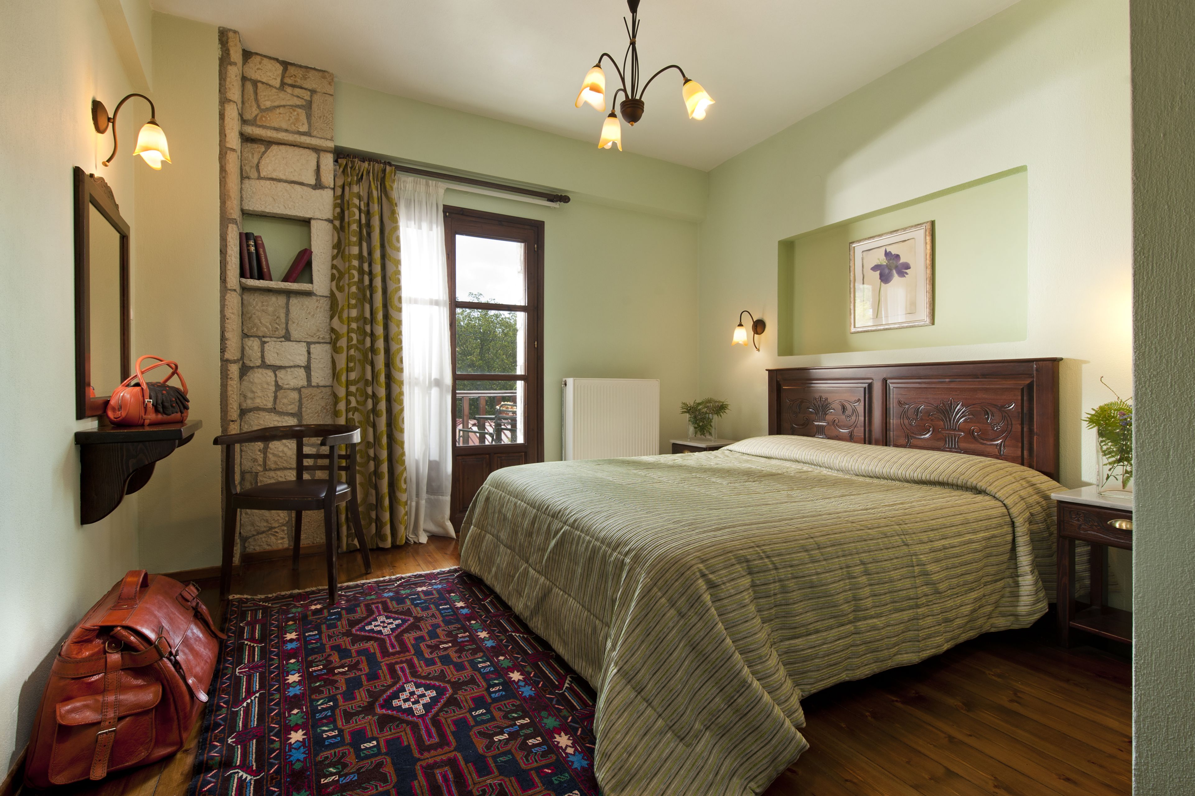 A bedroom with a bed, a chair, a rug, a suitcase, and a stone wall.