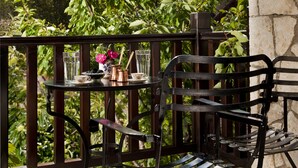 A balcony with a table and a chair, surrounded by greenery and a stone wall. - Fretzato Traditional Guest House (Pyli)