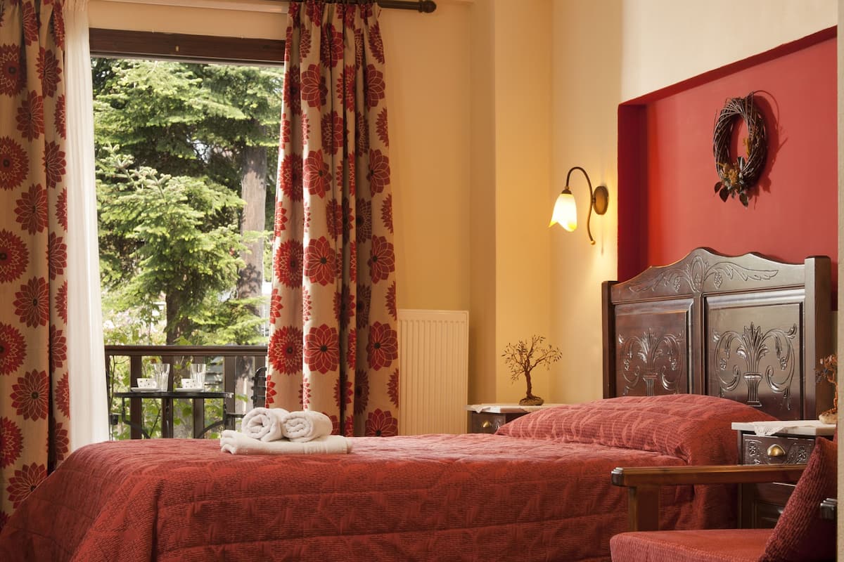 A bedroom with a large bed, a chair, a dresser, a window with curtains, and a chandelier.