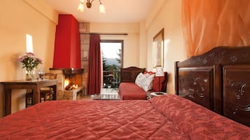 A bedroom with a large bed, a fireplace, a table with a vase of flowers, and a view through a window.