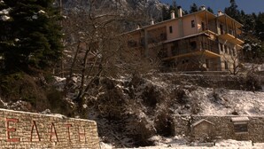 A multi-story building with a stone facade, located on a hillside with snow-covered trees and a clear sky. - Kroupi Hotel (Pyli)