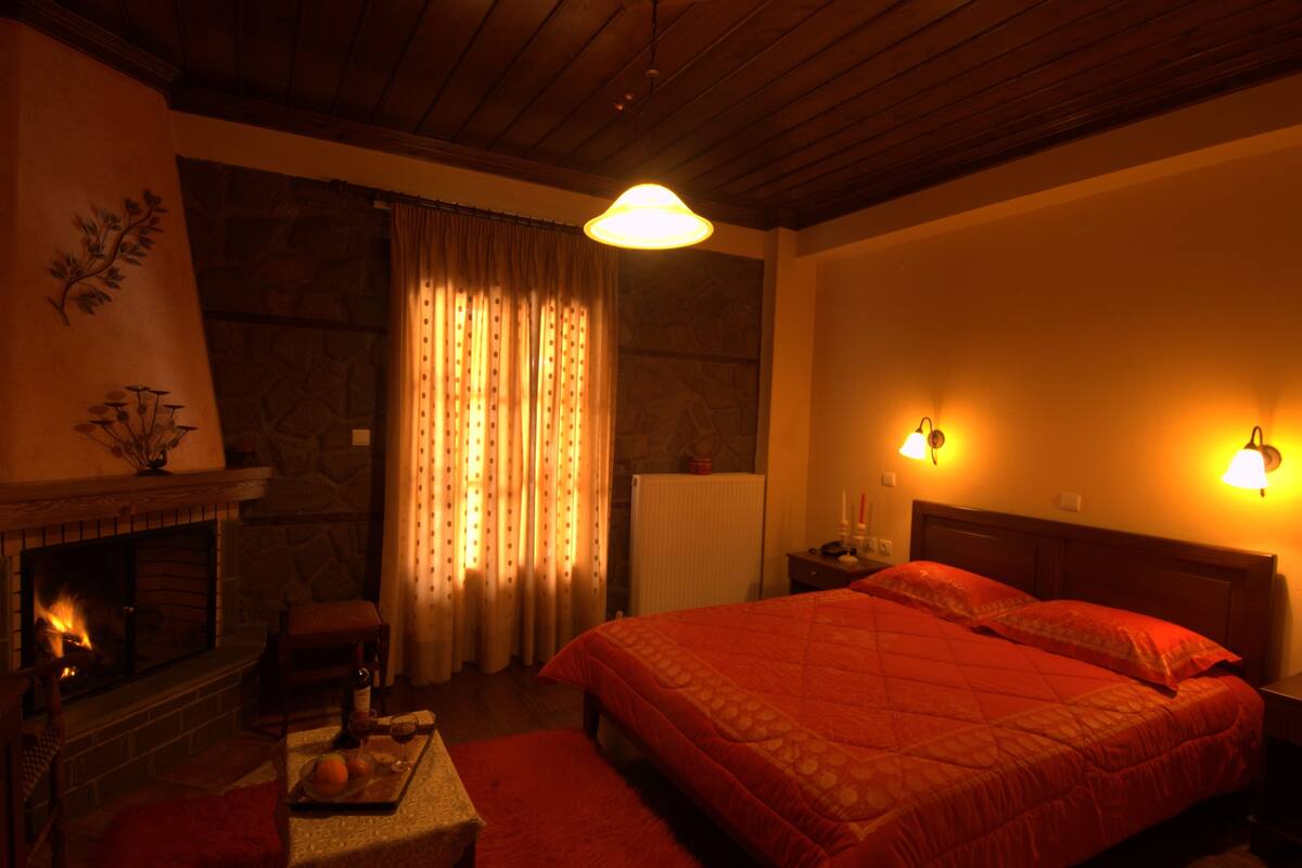 Une chambre confortable avec une cheminée, un grand lit avec une literie rouge et deux lampes fixées au mur.