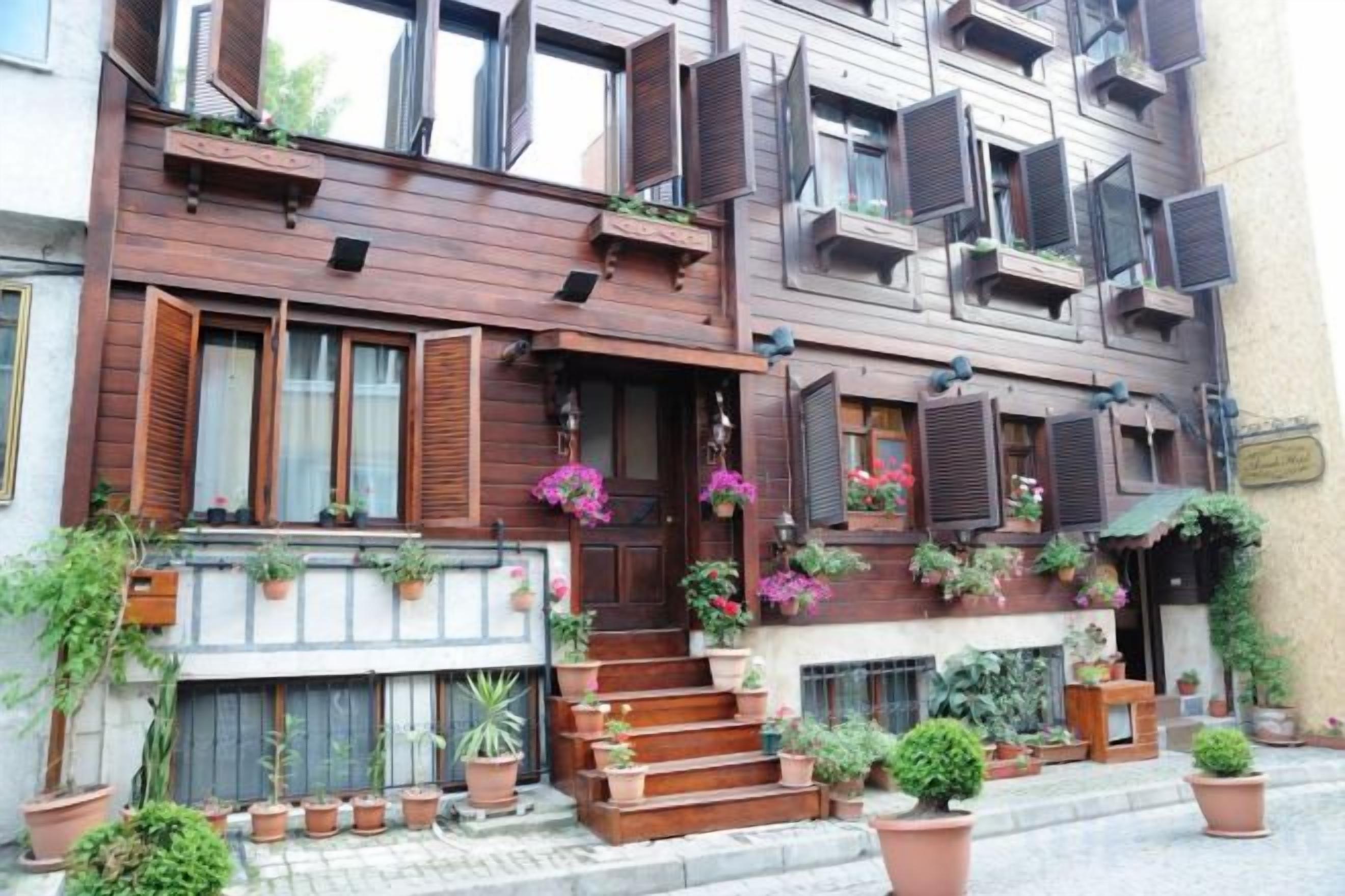 A multi-story building with wooden balconies, potted plants, and a staircase leading to the entrance.