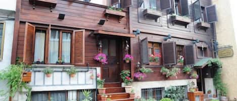 A multi-story building with wooden balconies, potted plants, and a staircase leading to the entrance.