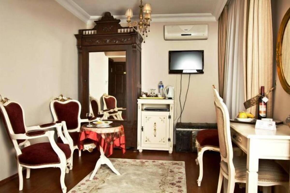 A room with a dining table, chairs, a television, a mirror, and a chandelier.