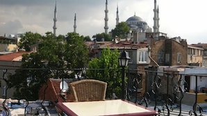 Un balcó amb mobiliari de vimetes, vista d'una mesquita amb minarets i edificis circumdants.