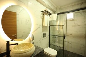 A bathroom with a round mirror, a bowl sink, a toilet, and a glass-enclosed shower. - Asmali Hotel (Istanbul)