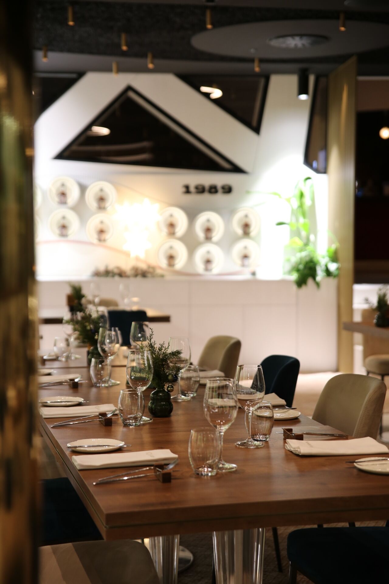 A dining table set with wine glasses, plates, and cutlery, with a modern interior design and a wall displaying vintage light bulbs.