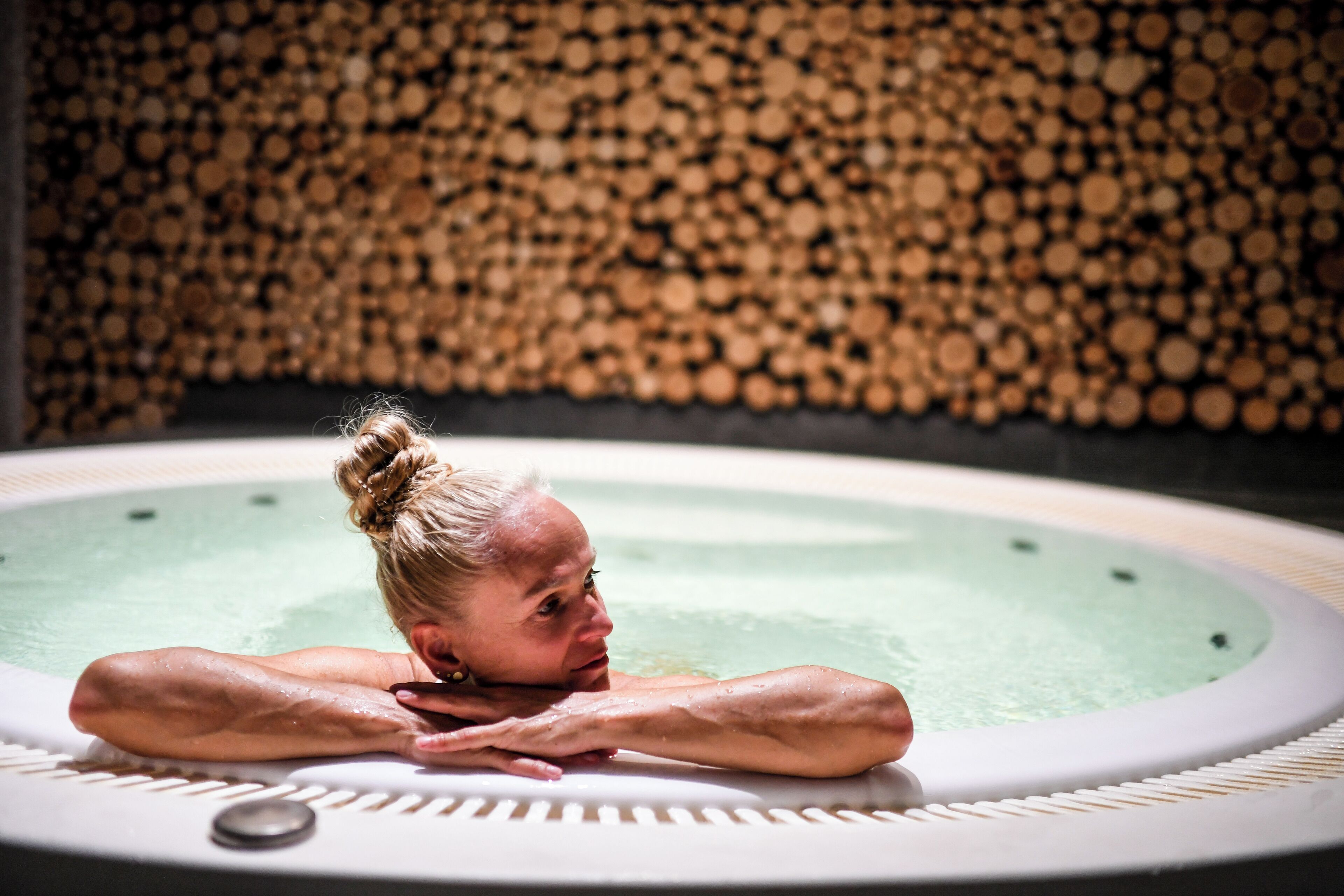 Una persona relajándose en un jacuzzi con un fondo de leña apilada.