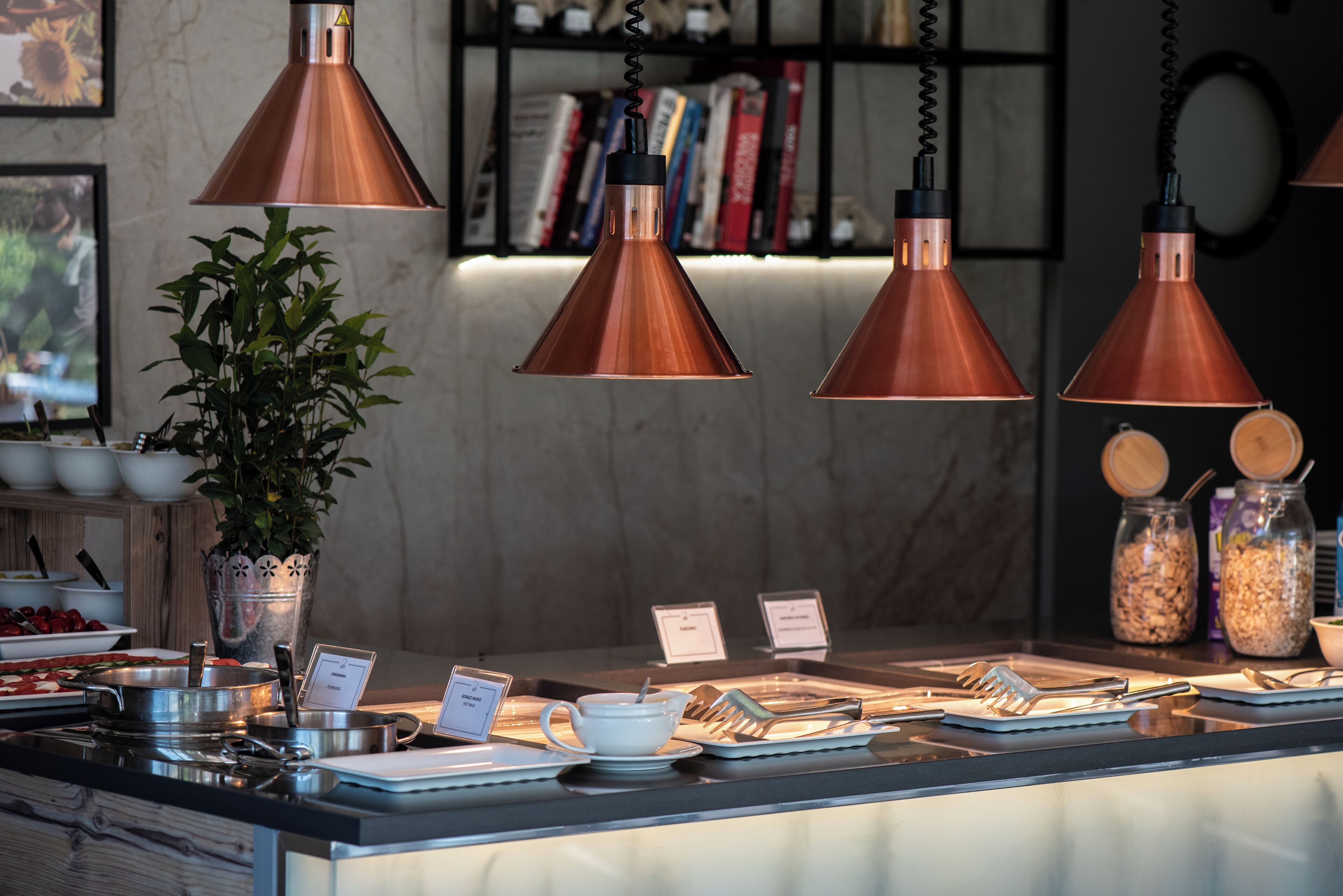 A breakfast bar with copper pendant lights, a potted plant, and various breakfast items.