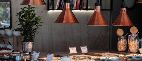 A breakfast bar with copper pendant lights, a potted plant, and various breakfast items.