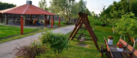 Un parque con un columpio, una zona de juegos techada y una mesa de picnic con flores.