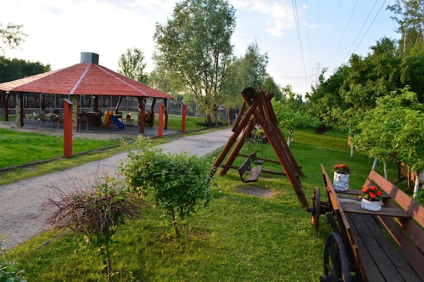A park with a swing set, a covered play area, and a picnic table with flowers.