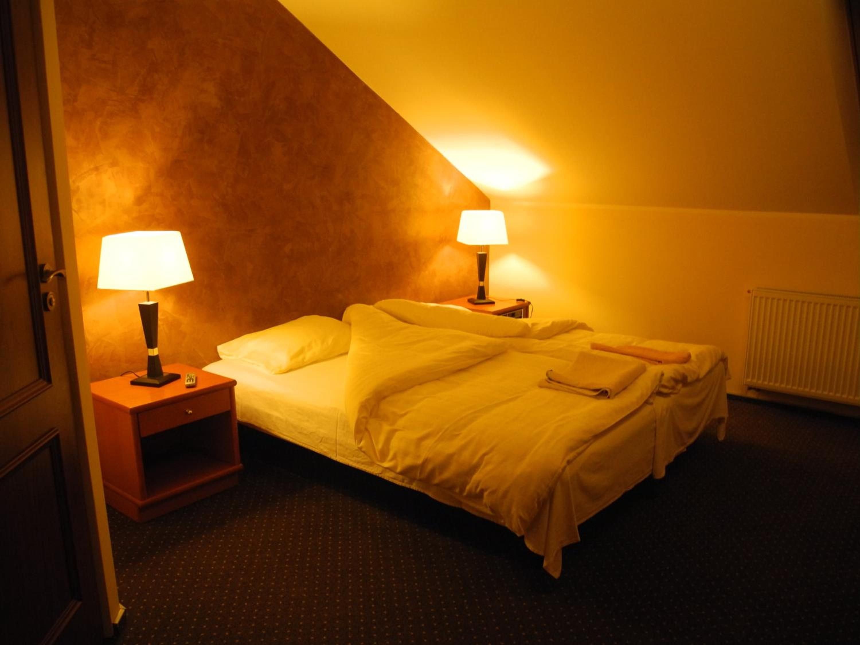 A hotel room with a bed, two bedside lamps, a nightstand, and a radiator.