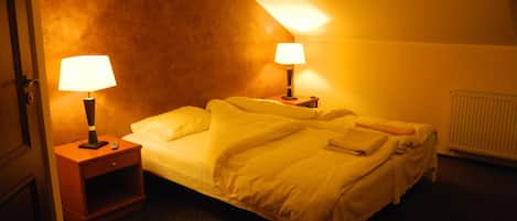 Una camera d'albergo con un letto, due lampade da comodino, un comodino e un termosifone.