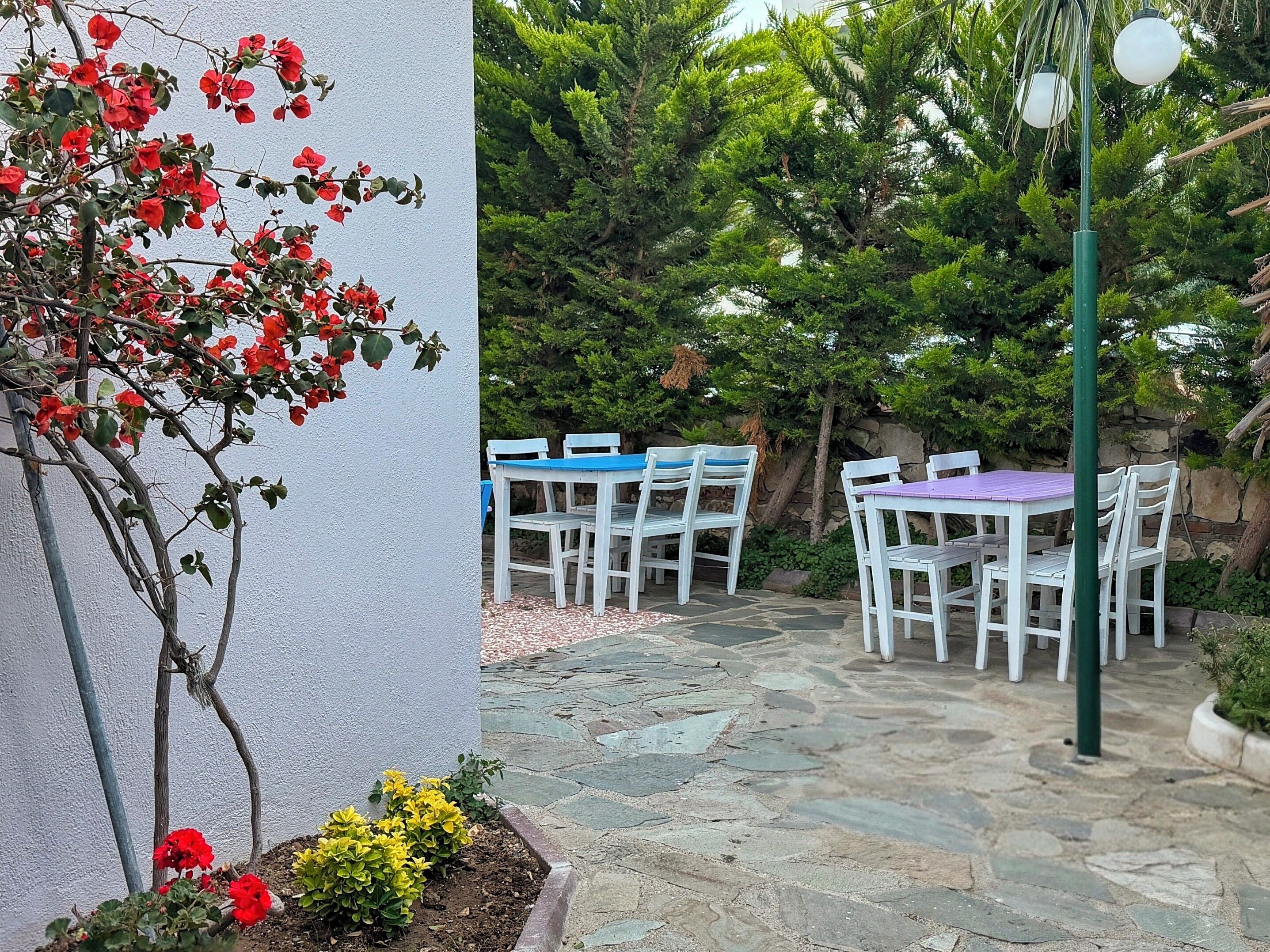 An outdoor patio with stone flooring, white chairs, and a table with a blue and purple tablecloth.