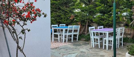 An outdoor patio with stone flooring, white chairs, and a table with a blue and purple tablecloth.