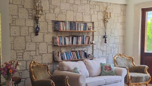 A living room with a stone wall, a bookshelf, a sofa, two armchairs, and a small table with a vase of flowers. - Karaburun Konak Hotel (Karaburun)