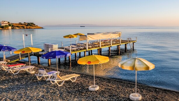 A pier with lounge chairs and umbrellas, a calm sea, and a distant landmass. - Karaburun Konak Hotel (Karaburun)