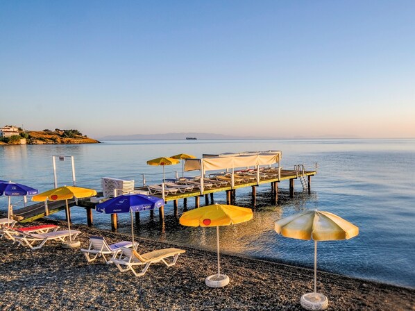 A pier with lounge chairs and umbrellas, a calm sea, and a distant landmass. - Karaburun Konak Hotel (Karaburun)