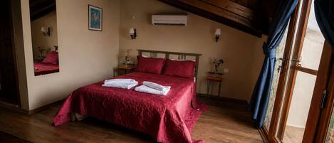 A bedroom with a wooden ceiling, a bed with red bedding, a mirror, and an air conditioning unit.