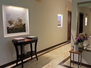 Un couloir orné de tableaux encadrés, une console sur laquelle sont posés des livres, un miroir et une petite table agrémentée de fleurs.