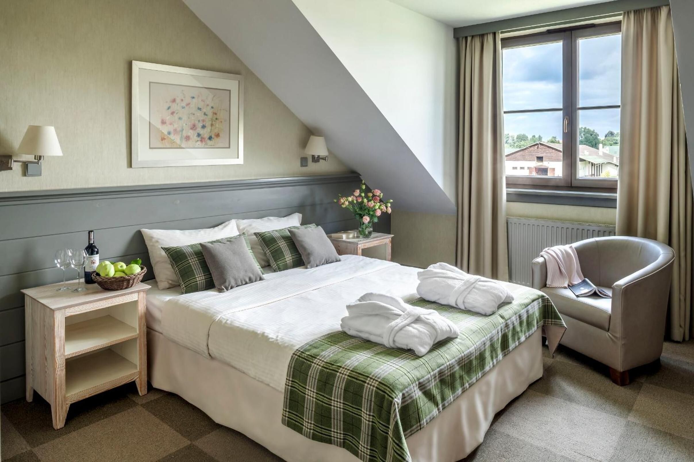 A neatly arranged hotel room with a large bed, a chair, a nightstand with a lamp, and a window with curtains.