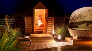 A wooden structure with a thatched roof, a wooden sauna, and a wicker lounge chair with cushions. - Sielanka nad Pilicą (Warka)