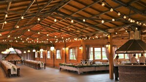 A spacious hall with long tables set for dining, a kitchen area, and a high ceiling with exposed beams and hanging lights. - Sielanka nad Pilicą (Warka)