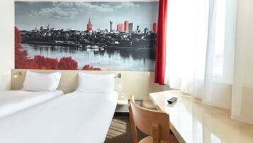 Habitación de hotel con cama, escritorio, silla y un gran mural de paisaje urbano en la pared.