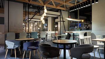 A modern cafe with round tables and chairs, exposed ceiling beams, and pendant lighting.